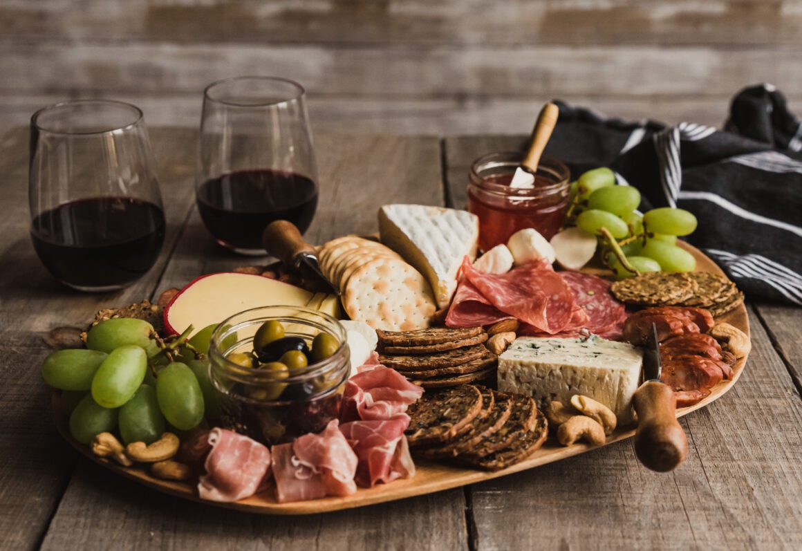 Close up of charcuterie board and glasses of wine on wooden tabl Cheese and meat platter with wine.
